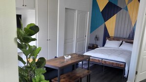 Un dormitorio acogedor con cama, una mesita con banco, una planta en maceta y una pared con estampado geométrico.