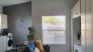 Un espacio habitable pequeño con sofá, una mesa de centro, lavadora y ventana con persianas.