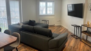 Un salon moderne avec un canapé d’angle, un téléviseur à écran plat et un coin repas.