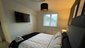 Une chambre à coucher avec un lit, un téléviseur fixé au mur, une fenêtre avec des stores et une lampe de chevet.