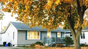 A two-story house with a front porch and a tree with autumn leaves. - Private Lakefront House with Hot Tub, Kayaks and Beach (Selkirk)