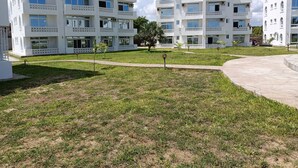 Un immeuble résidentiel moderne à plusieurs étages, doté de balcons, d’une pelouse bien entretenue et surplombant un ciel dégagé.