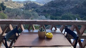 Una mesa con un cactus en maceta y una maceta amarilla sobre una terraza de madera con vista a un paisaje montañoso.