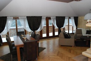 A spacious living room with a wooden floor, a dining table with chairs, a sofa, and a balcony with curtains. - Star Hamry Mosl590 (Staré Hamry)