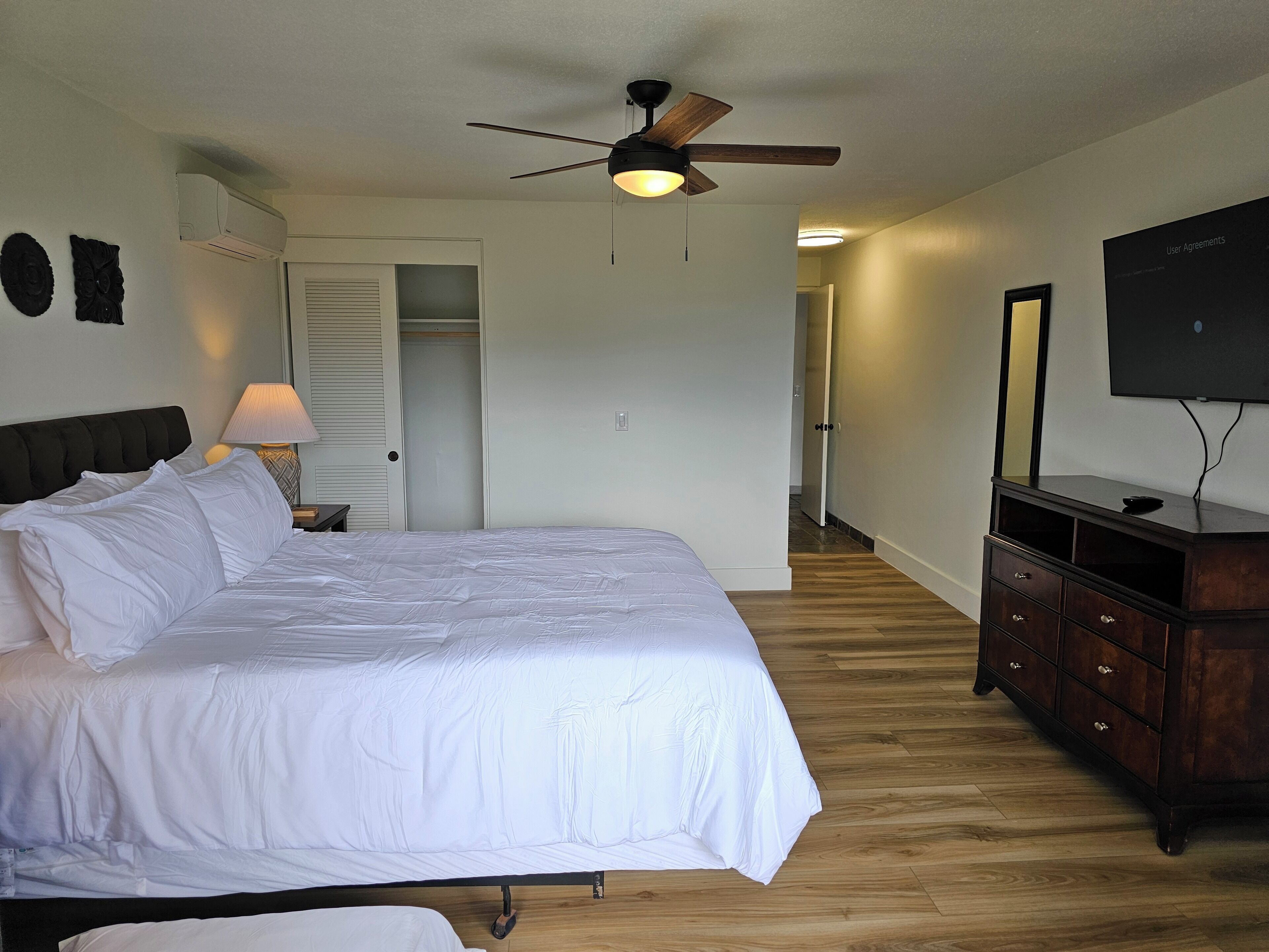 A bedroom with a bed, a ceiling fan, a dresser, and a television.