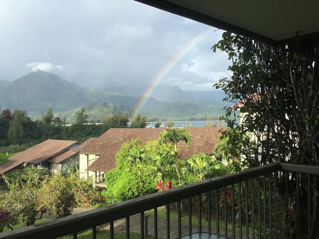 A view from a balcony with a rainbow, houses, and mountains in the background.