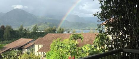 A view from a balcony with a rainbow, houses, and mountains in the background.