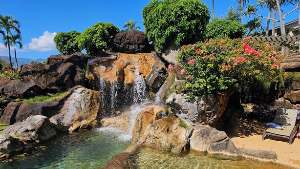 Una piscina cristalina con cascada, rodeada de rocas y vegetación.