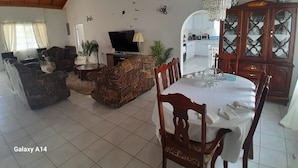 Un amplio salón con una mesa de comedor, sillas, un televisor y una araña.