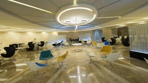 Une salle de conférence moderne dotée d’un luminaire circulaire au plafond, de plusieurs configurations d’assises et d’un sol en marbre.