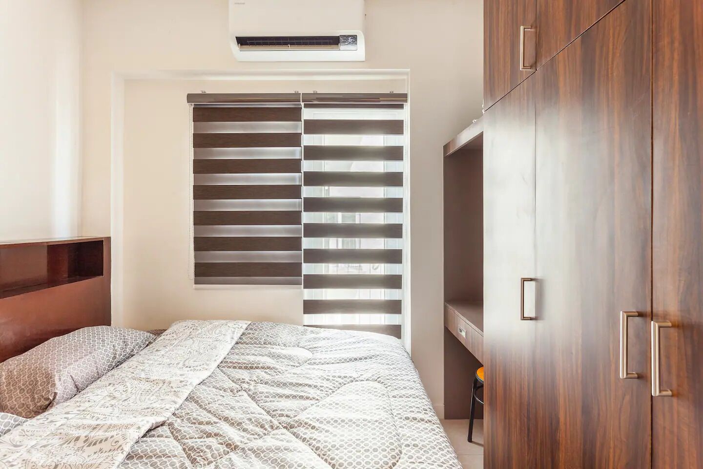 A bedroom with a bed, a wardrobe, and a window with blinds.