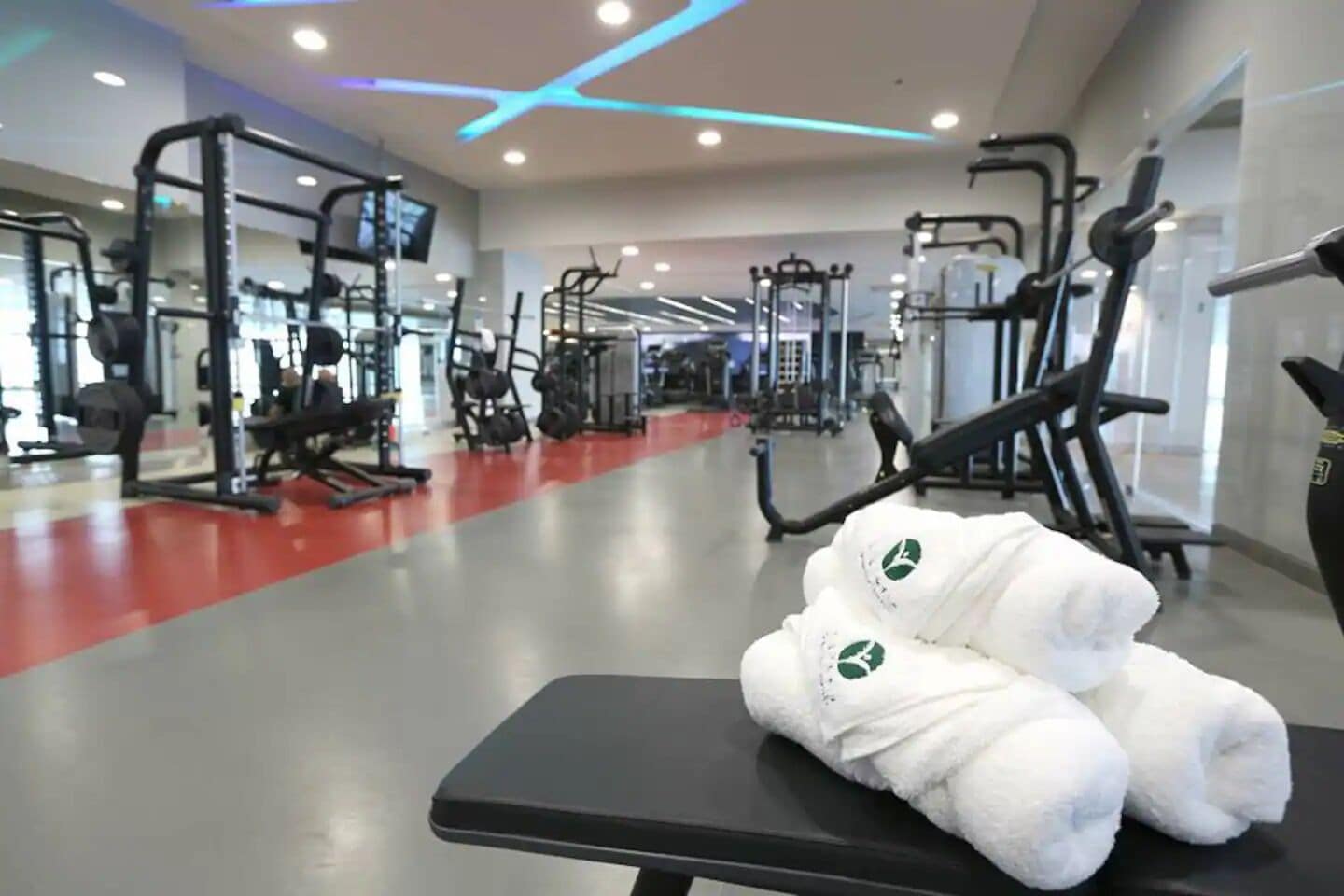 A gym with various exercise equipment, a bench with towels, and a red floor.