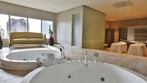 Une salle de bain moderne avec une grande baignoire, un canapé et une petite table sur laquelle sont posées des serviettes.