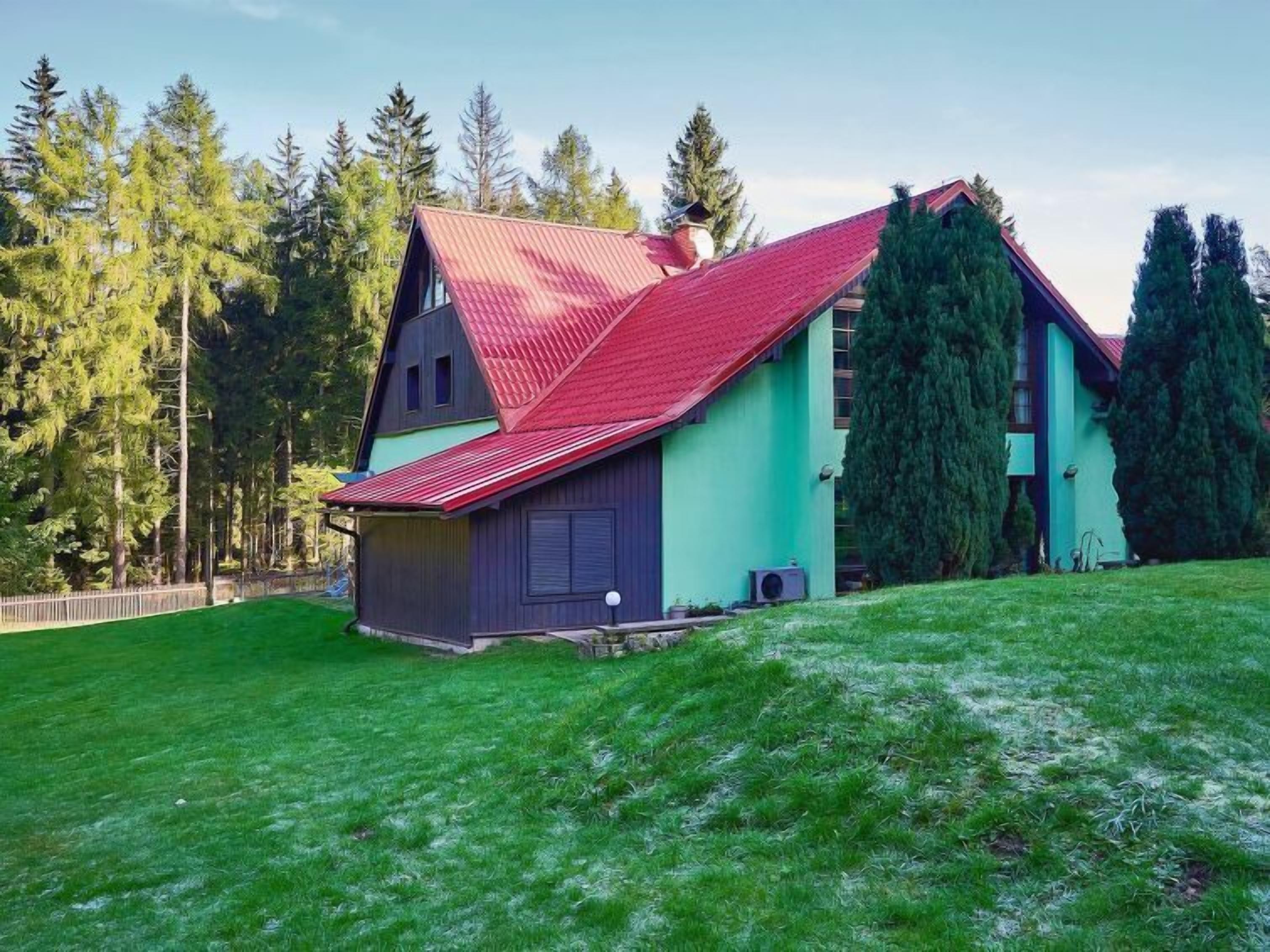 Une maison à deux étages, avec un toit rouge, entourée d’une pelouse verdoyante et de grands arbres.