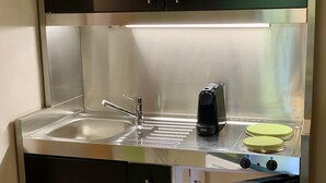Een kleine keukenhoek met een roestvrijstalen spoelbak, een koffiezetapparaat en twee elektrische kookplaten.