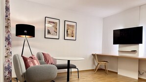 Een moderne woonkamer met een bank, een klein rond tafeltje, een televisie en twee ingelijste foto’s aan de muur.