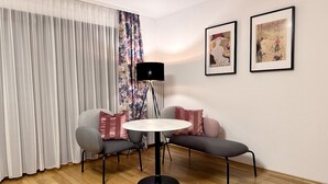 Een kamer met een ronde tafel, twee grijze banken, een vloerlamp en twee ingelijste foto's aan de muur.
