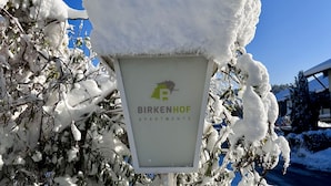 Une enseigne pour les appartements Birkenhof, avec un toit et des branches couverts de neige.