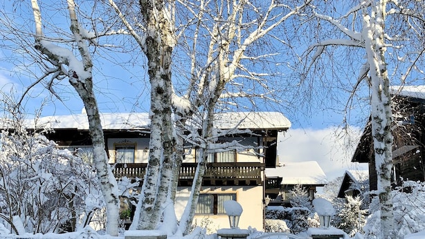Un bâtiment enneigé, doté d’une entrée en pierre, de balcons en bois et surplombant un ciel dégagé.