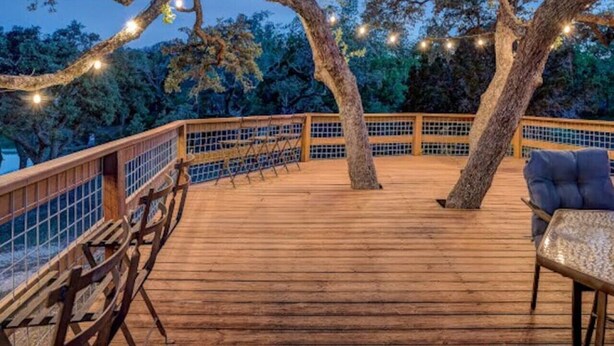 Una terraza de madera con barandilla, una mesa y sillas.