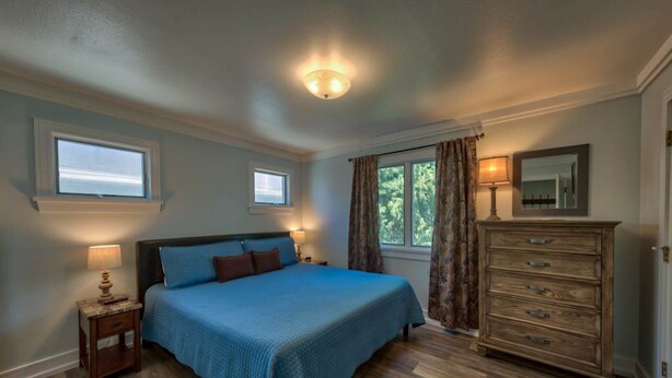 Quarto com cama grande, penteadeira, mesa de cabeceira e duas janelas.