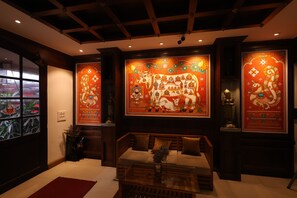 A room with a traditional design, featuring a sofa, a glass coffee table, and a large wall mural with religious figures. - Kovilakam Residency Private Limited (Kozhikode)