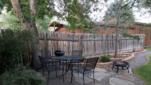 Une terrasse avec une table et des chaises en pierre, entourée d’une clôture en bois et de verdure.