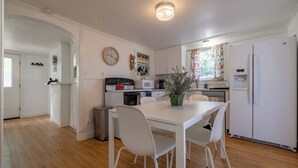 Une cuisine moderne avec des meubles blancs, une table à manger avec des chaises, une horloge au mur et un réfrigérateur.