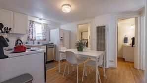 Une cuisine moderne avec des meubles blancs, une bouilloire rouge et un coin repas comprenant une table et des chaises blanches.