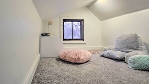 A small, well-lit attic room with a sloped ceiling, a window, and a cozy seating area with a bean bag and pillows.
