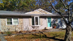 A single-story house with a stone facade, a front porch, and a front door with a green accent.