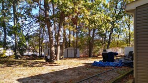 A backyard with a gravel path, trees, and a covered grill area.