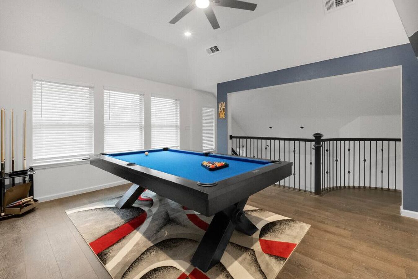 A pool table in a room with a high ceiling, large windows, and a balcony with a railing.