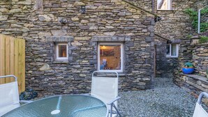 A stone building with a small window and a door, a round glass table with a chair, and a wooden fence. - Laburnum Cottage -  Windermere, with Parking (Windermere)