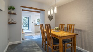 A dining area with a wooden table and chairs, a hanging light fixture, and a heart-shaped decoration on the wall. - Laburnum Cottage -  Windermere, with Parking (Windermere)