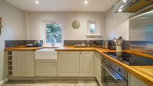 A modern kitchen with white cabinetry, a wooden countertop, a stainless steel range hood, and a built-in oven. - Laburnum Cottage -  Windermere, with Parking (Windermere)