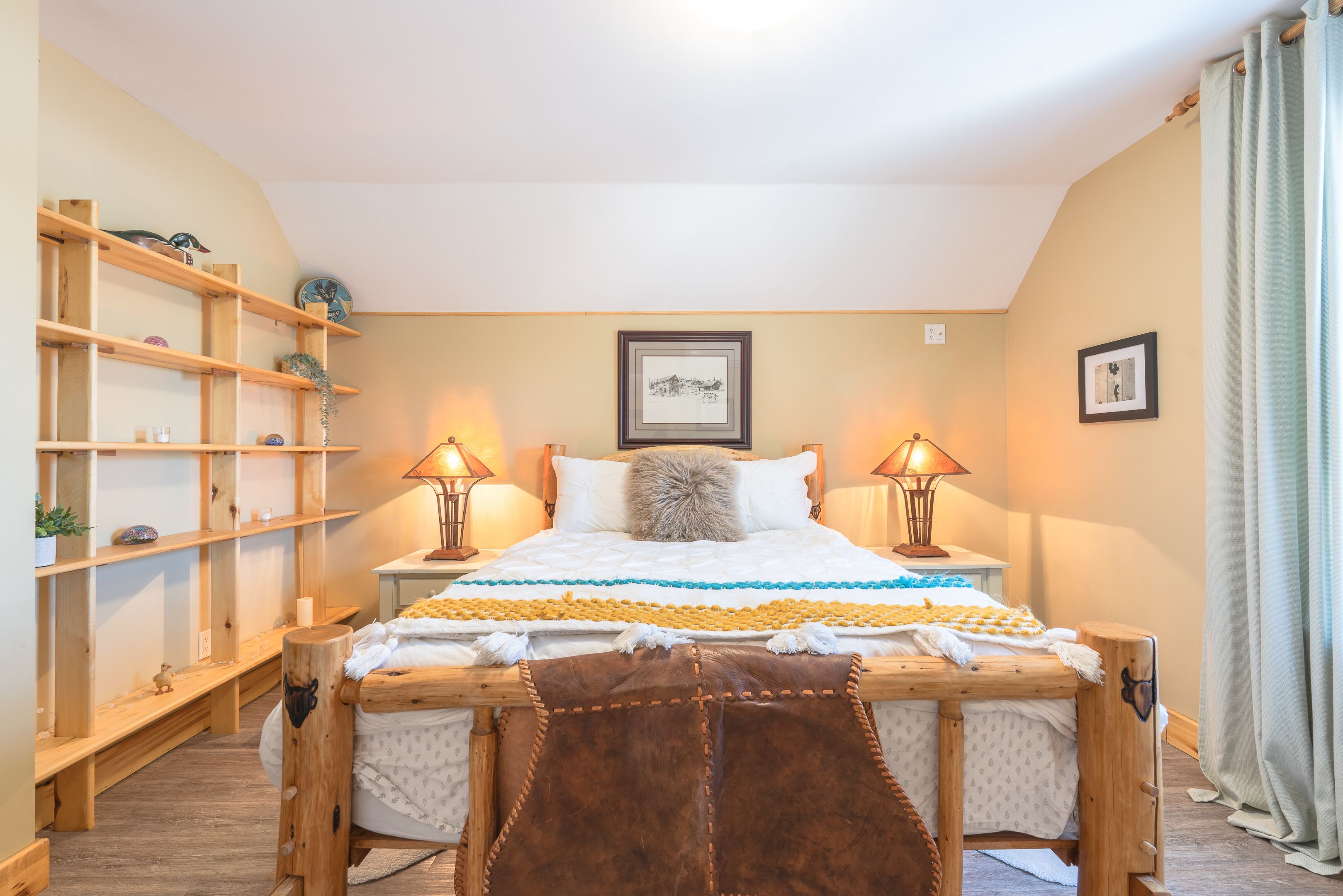 A cozy bedroom with a wooden bed, a shelf unit, and two lamps.