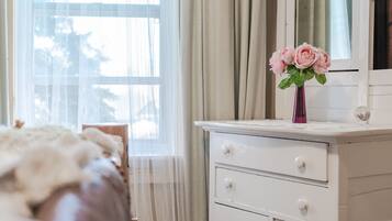 Une chambre à coucher avec un lit, une commode, un vase de fleurs et une fenêtre avec des rideaux.
