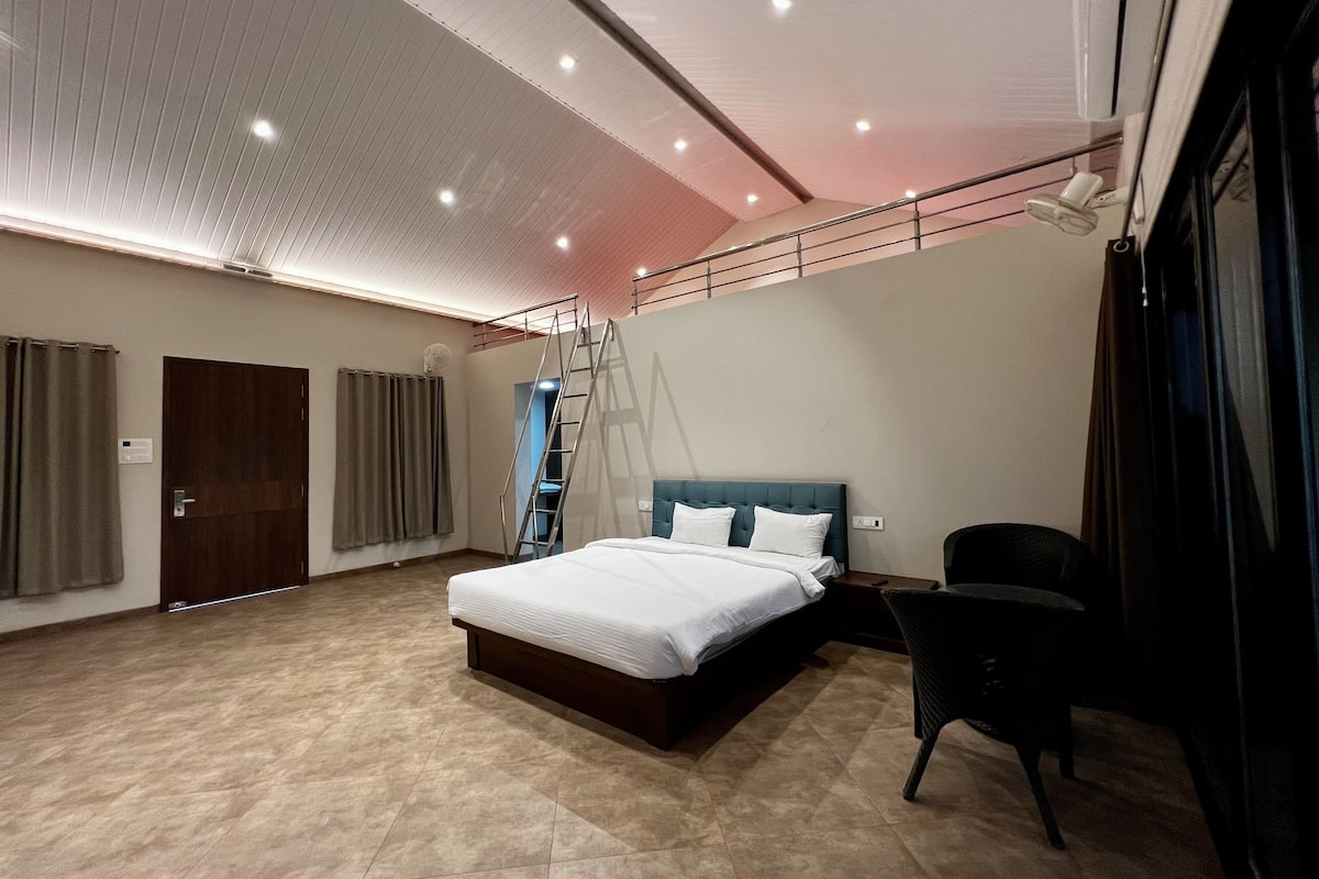 Une chambre d’hôtel moderne avec un grand lit, une chaise, une échelle et une vue sur le ciel par la fenêtre.