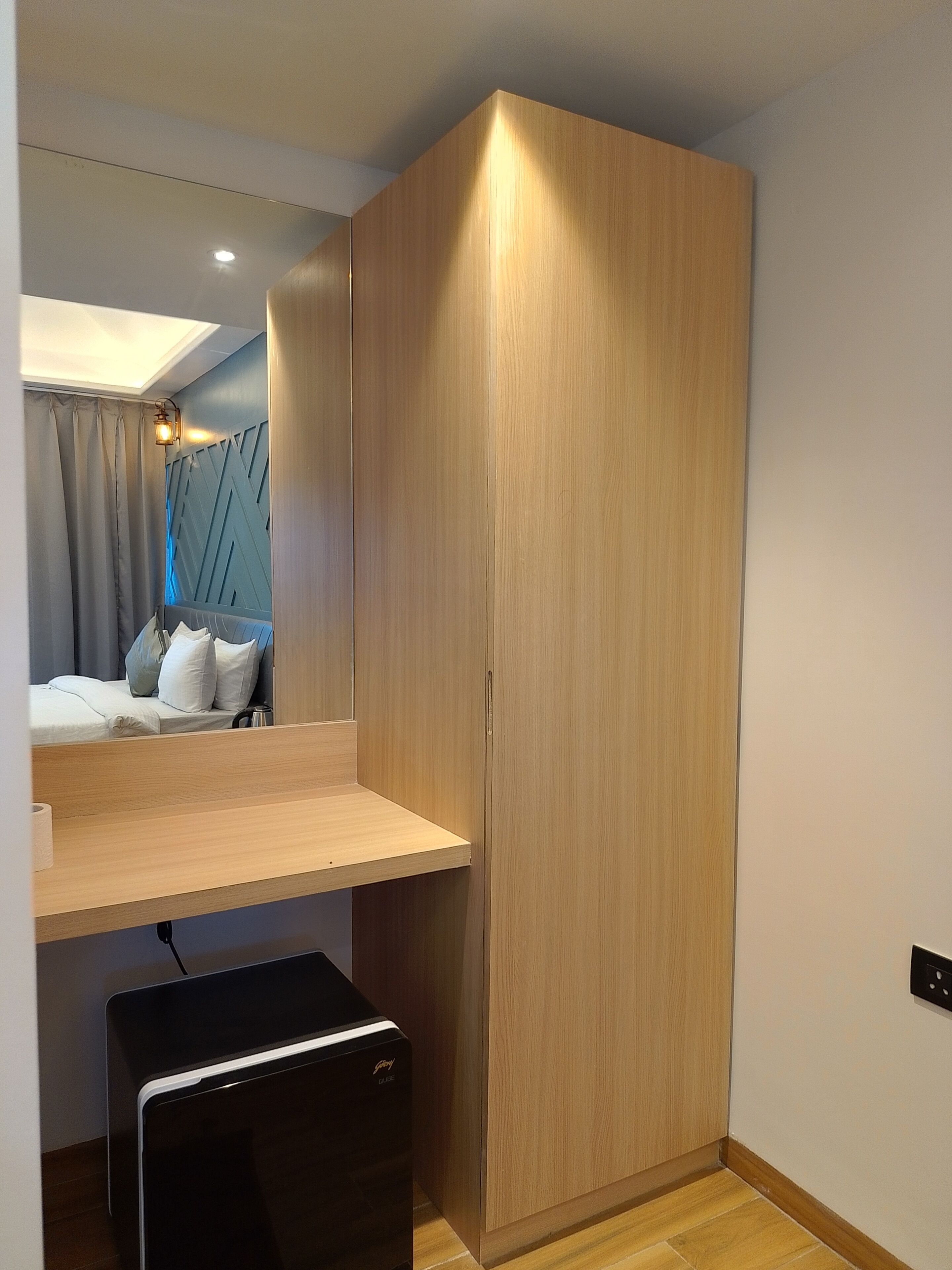 A compact room with a bed, a wooden wardrobe, a small desk, and a mirror.