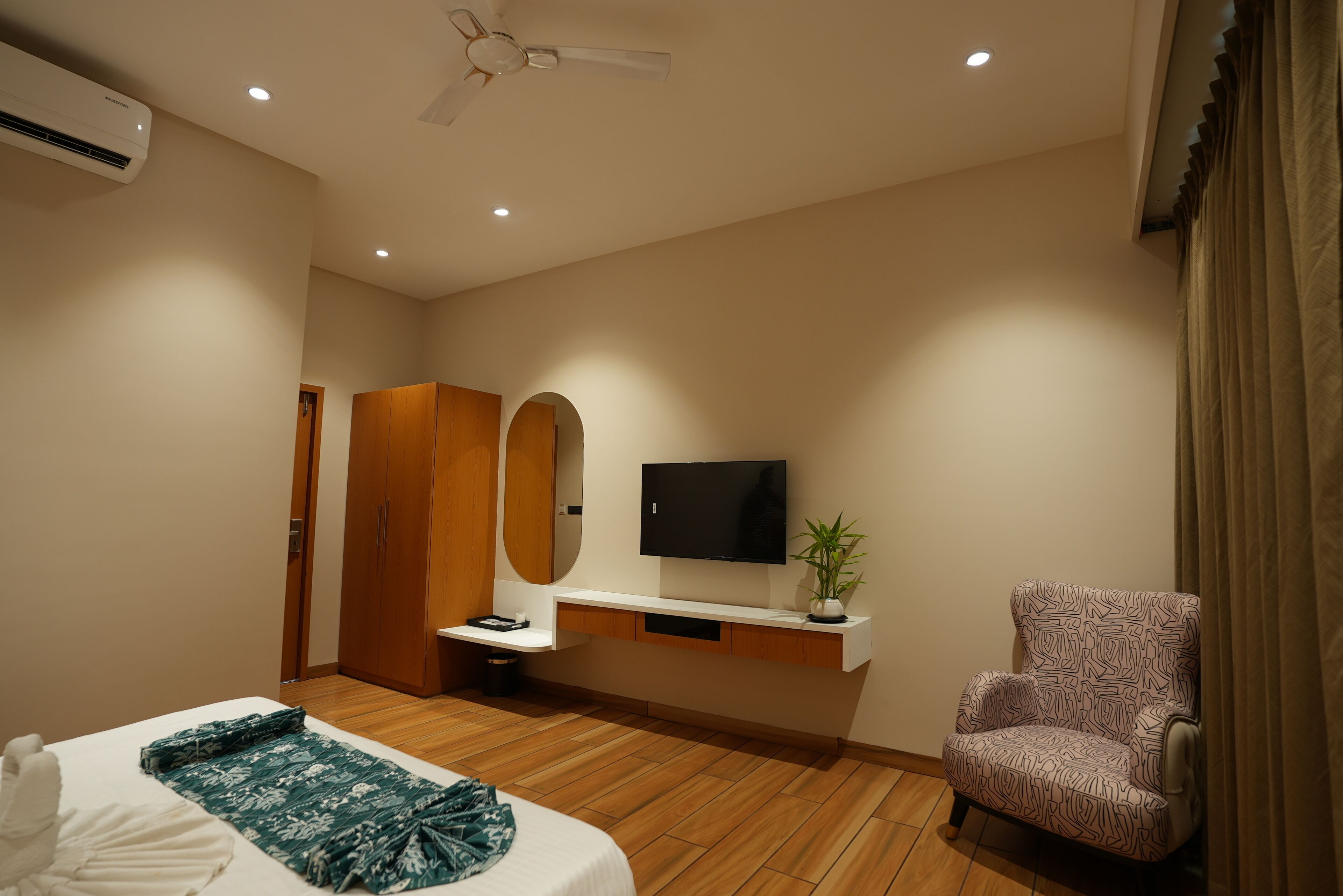 Une chambre d’hôtel moderne équipée d’un lit, d’une télévision, d’une plante, d’une chaise et d’une armoire.