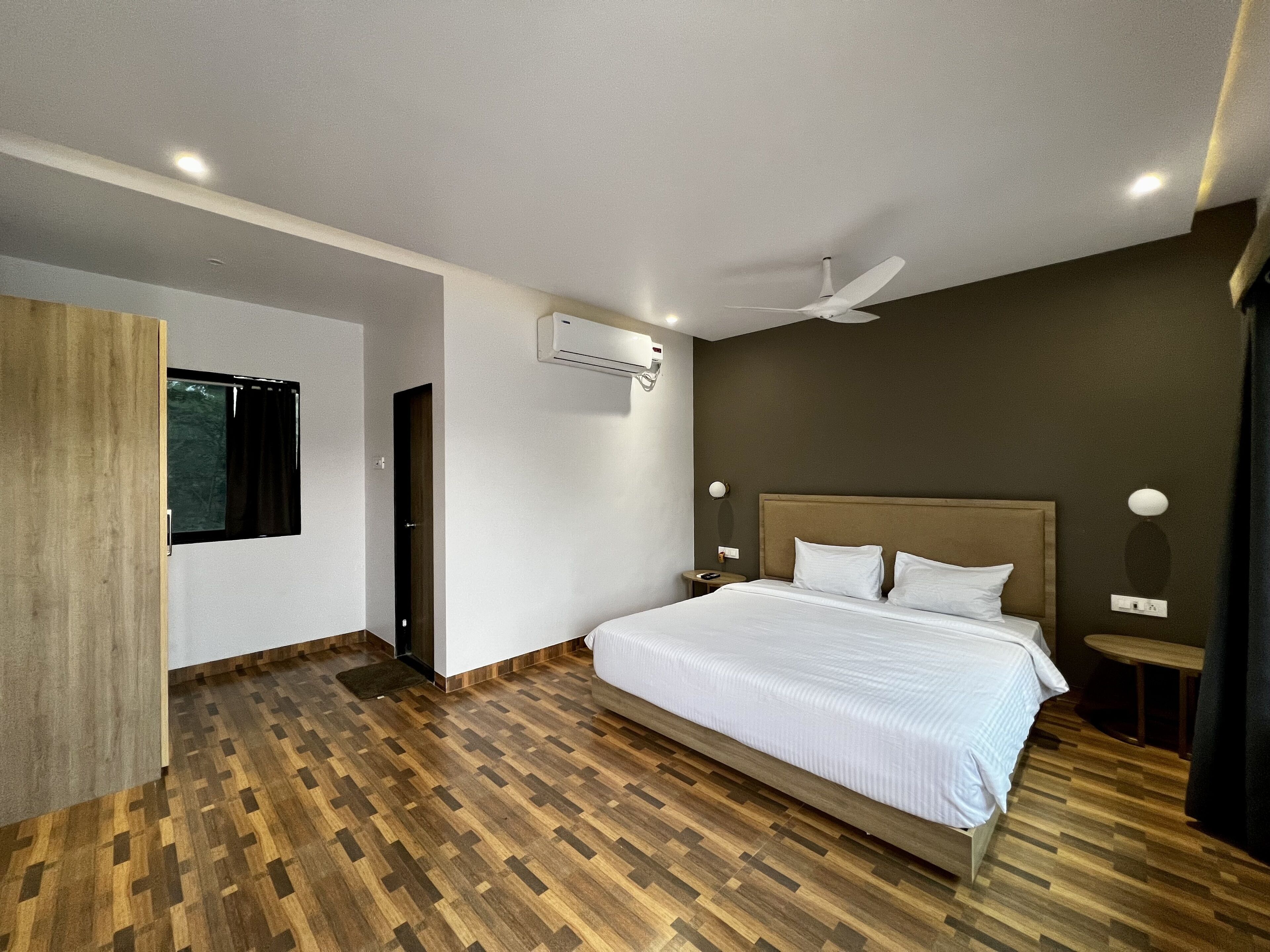 A modern hotel room with a wooden floor, a bed with white linens, a ceiling fan, and a window with curtains.