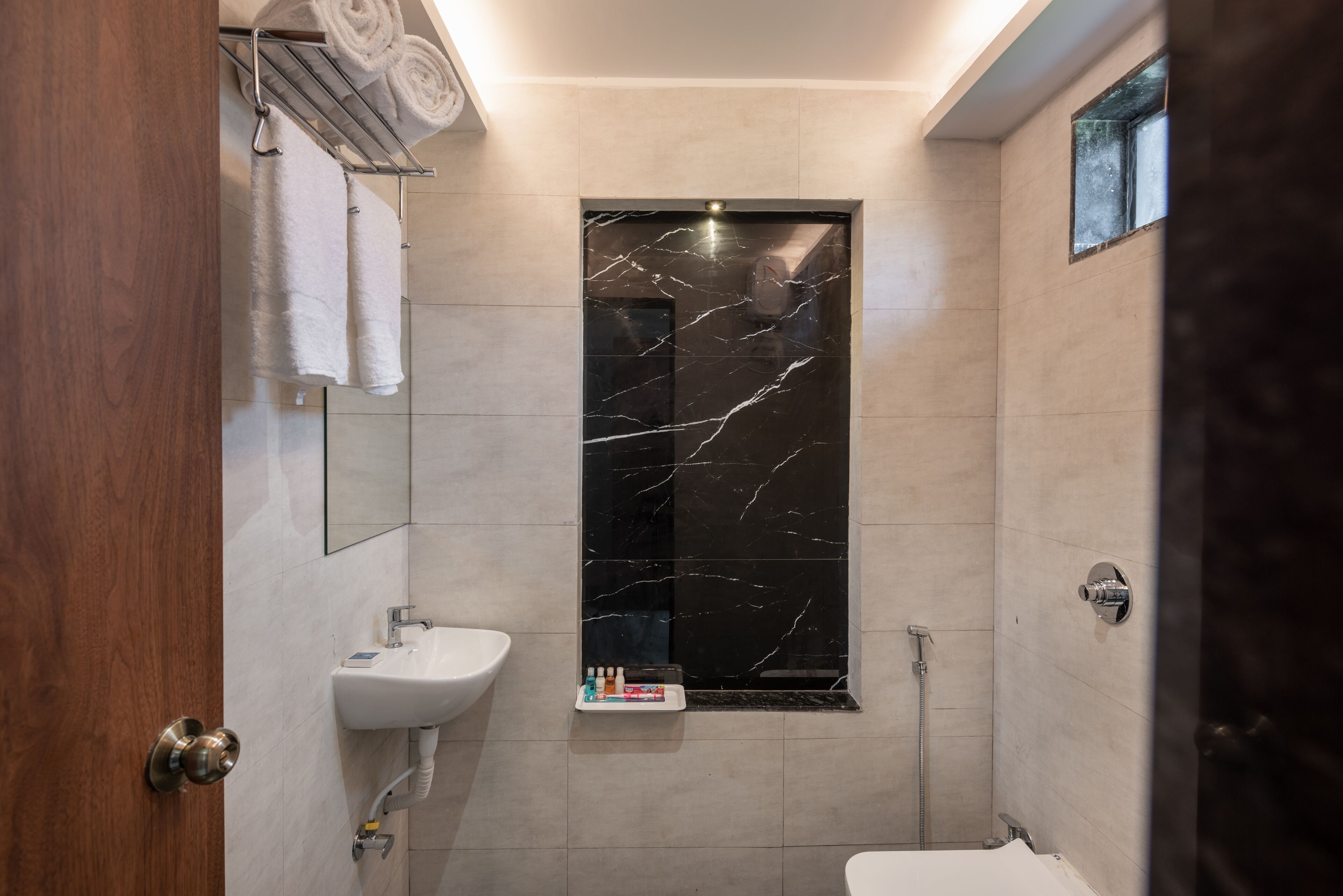 A modern bathroom with a marble shower wall, a white sink, and a toilet.