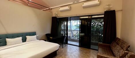 Habitación de hotel con cama, una mesita, una silla y balcón con vistas a árboles.