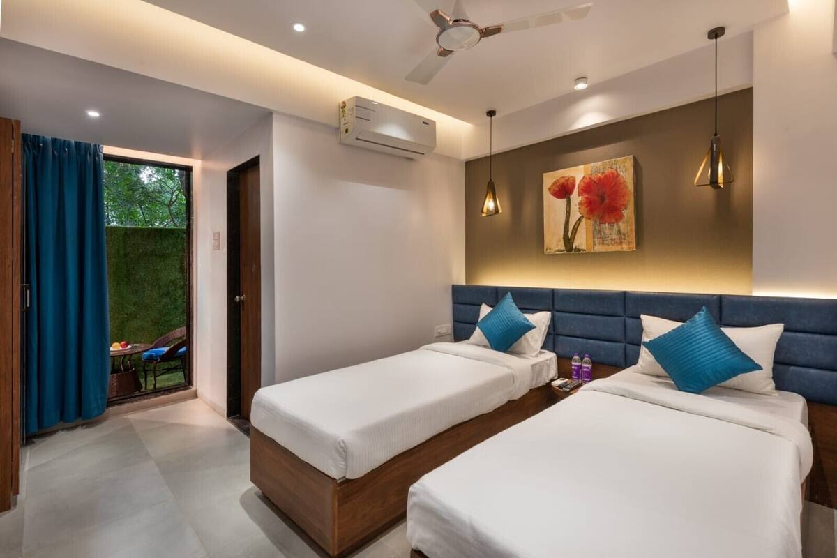 Une chambre d’hôtel moderne avec deux lits simples, un ventilateur de plafond, un appareil de climatisation et un tableau représentant des fleurs rouges au mur.