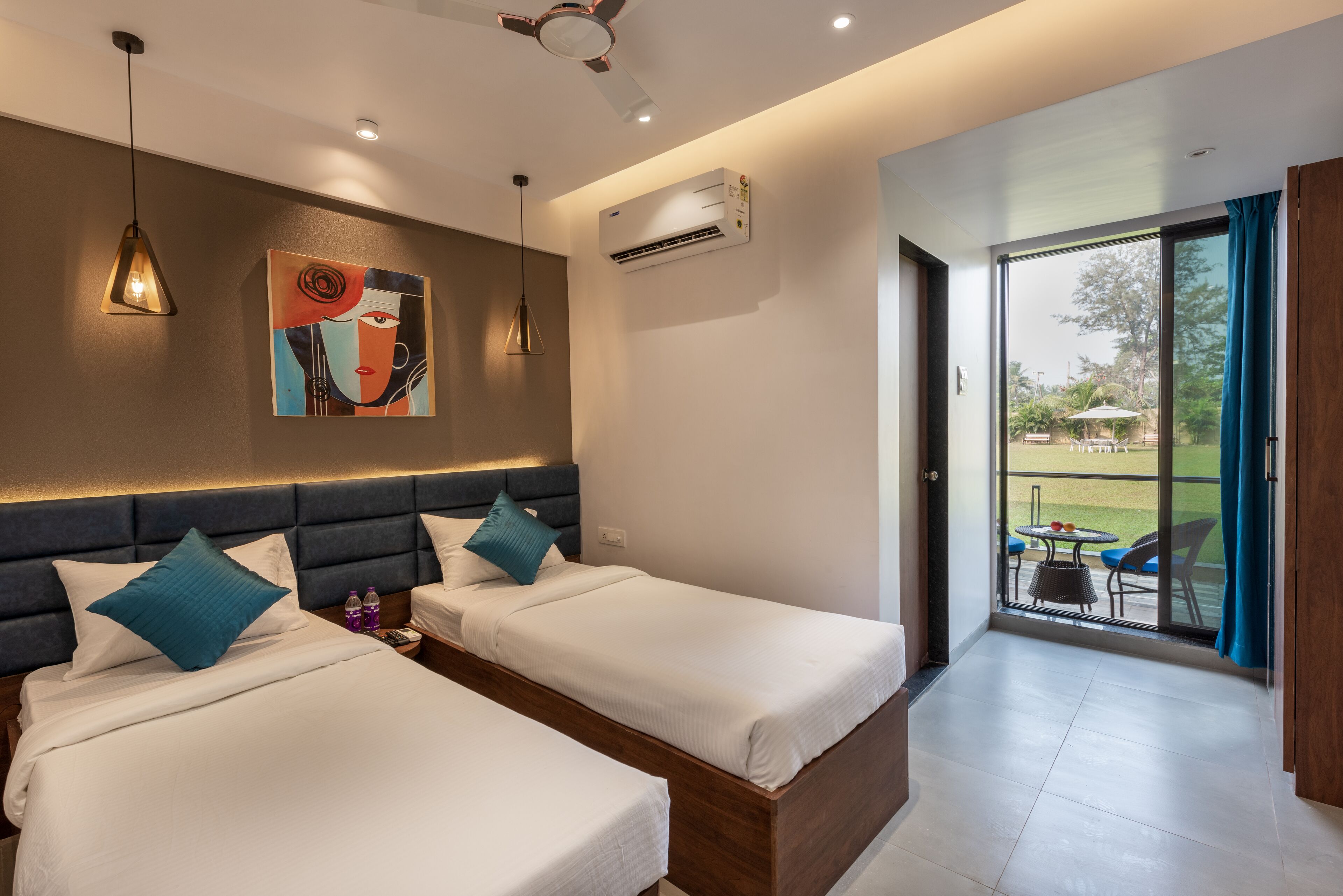 Una habitación de hotel moderna con dos camas, un ventilador de techo, un equipo de aire acondicionado y vistas al área exterior a través de una puerta de vidrio.
