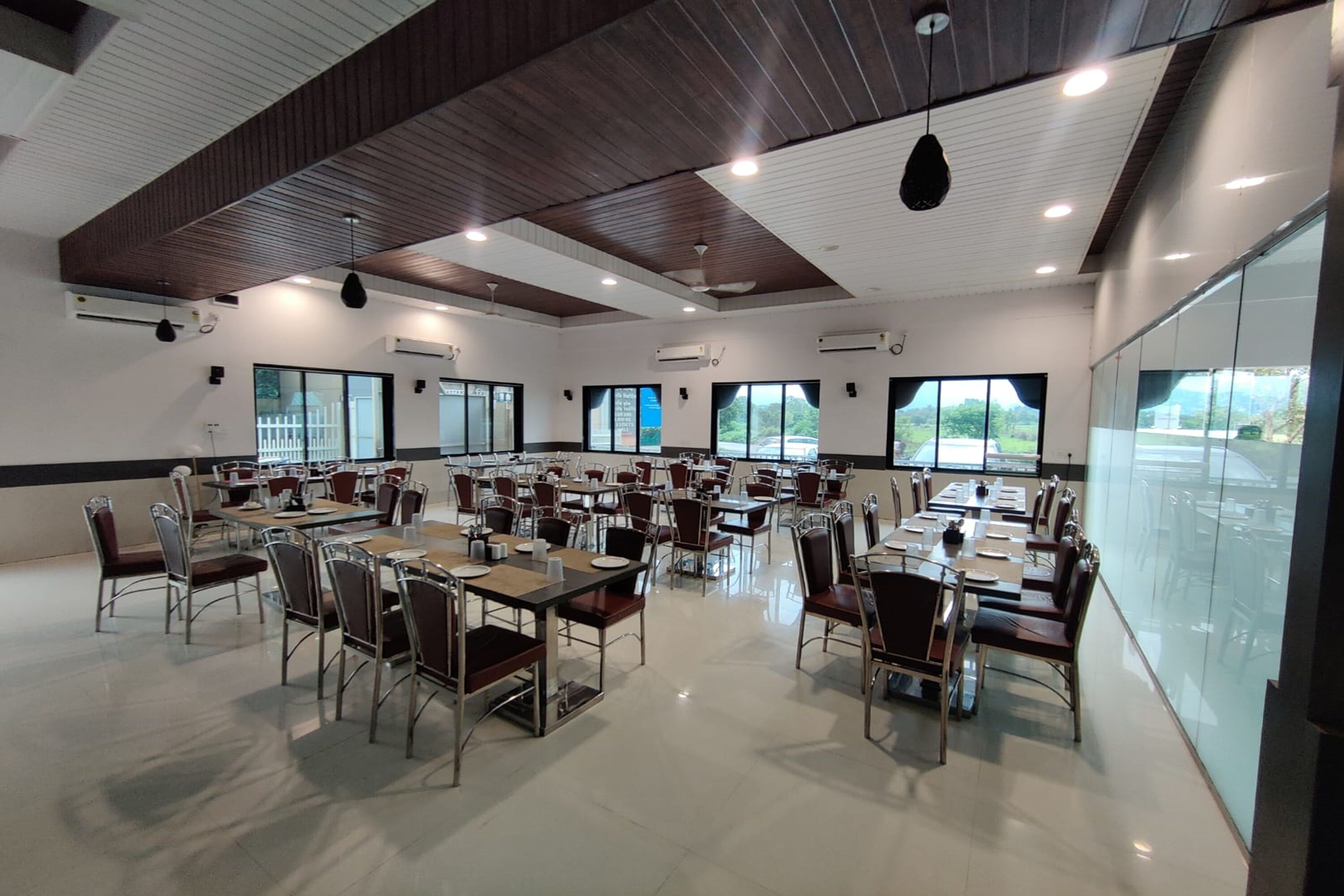 A spacious conference room with multiple tables and chairs, large windows, and ceiling fans.