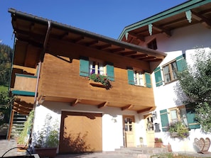 Un bâtiment traditionnel en bois, avec une porte en bois, des volets verts et un balcon agrémenté de jardinières.