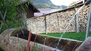 A rustic outdoor setting with a wooden water feature, a wooden structure, and a stack of firewood. - Apartment Bergzeit- 2 Per. 42sqm, 1 bedroom, wood stove, balcony, WLAN (Oberwössen)