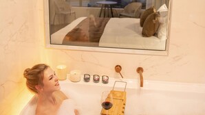 Une femme se détend dans une baignoire, avec vue sur une chambre à coucher par la fenêtre.